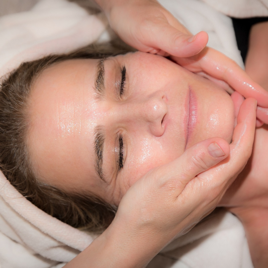 Une personne reçoit un massage facial relaxant avec des huiles, enveloppée dans une serviette blanche.