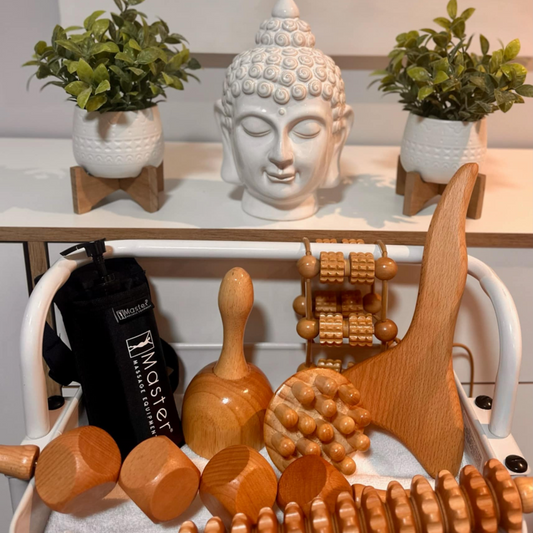 Collection d'outils de massage en bois pour la madérothérapie avec un buste de Bouddha et des plantes vertes.